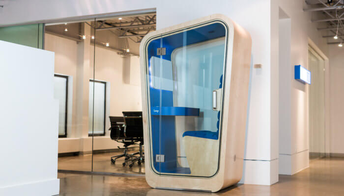 A Loop phone booth stands against a white wall at the corner of a hallway.