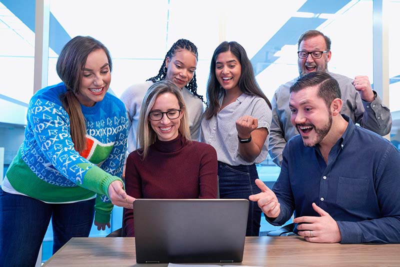  A team celebrates as they look at their coworker’s laptop in an office