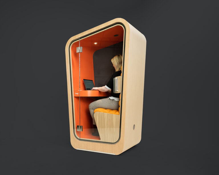 A Loop solo office pod with a orange interior and wood exterior and a woman working in it sits on a black background