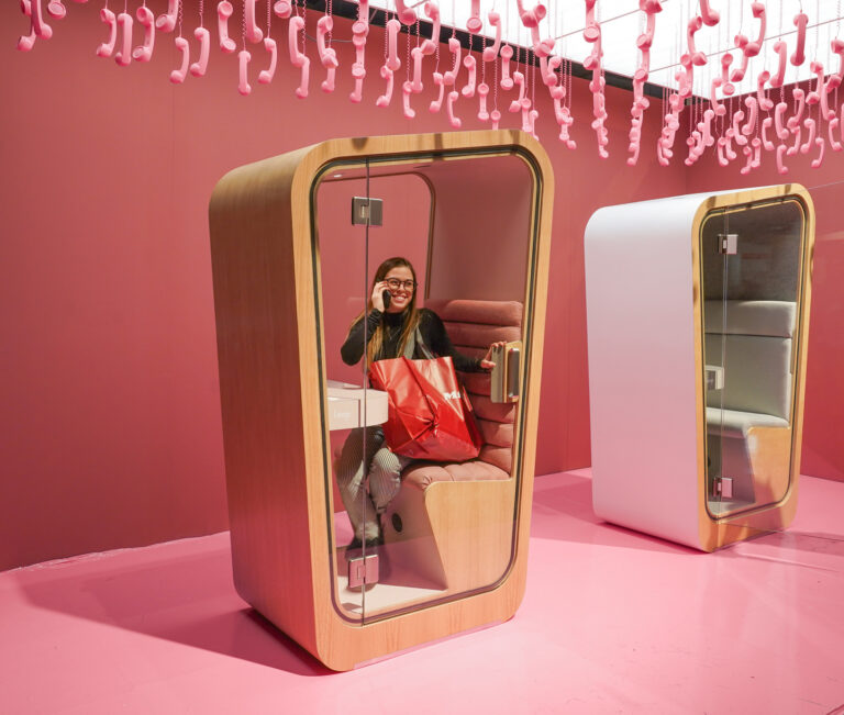 A pink interior loop solo phone booth in a tradeshow booth with hanging pink phones coming from the cieling