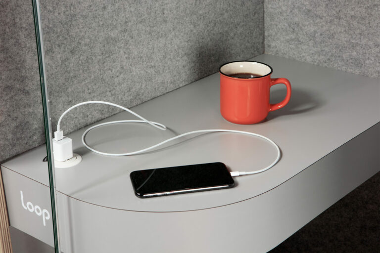 Loop phone booth counter top with a coffee and cellphone charging on top of it