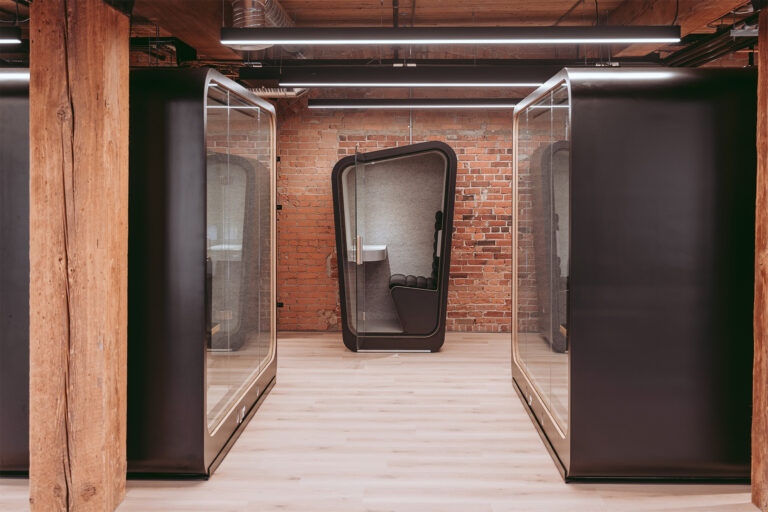a all black loop solo office pod sits in the middle of two loop access phone booths in a exposed brick open office
