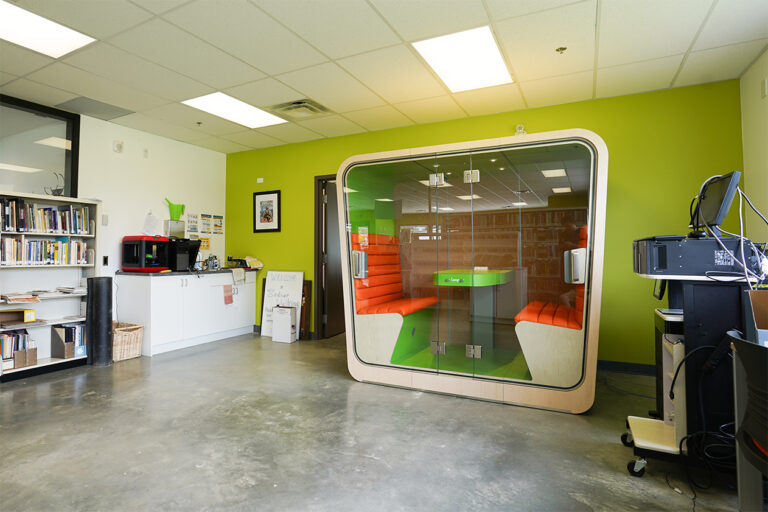 a vibrant colored loop cube privacy pod in a library with book shelves reflecting off the glass